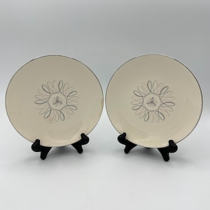 Puede incluir: Dos platos de cena de cerámica blanca con borde plateado y un diseño de espiral negro y gris en el centro.