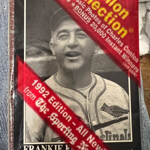 May include: A red, white, and yellow card with a picture of a baseball player in a white uniform with a red bird on the front. The card is from the 1992 edition of The Sporting News and features Frankie Frisch, a player for the St. Louis Cardinals. The card is part of a 18 card Conlon Collection.