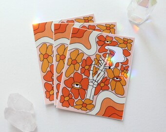 Peut inclure: Trois impressions d'art carrées avec un motif floral rétro orange, jaune et blanc. Chaque impression présente une main de squelette tenant une cigarette allumée, avec un graphisme d'œil. Le fond est rose clair.