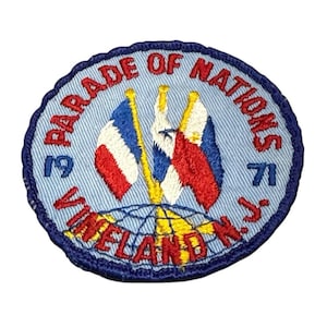 May include: Embroidered patch with a light blue background and a dark blue border. The patch features the text "PARADE OF NATIONS VINELAND N.J." and the years "19" and "71". Three flags are depicted in the center.
