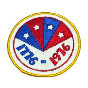 May include: Embroidered patch with a patriotic design. The patch features a circular shape with red, white, and blue segments, each with a white star. The text "1776 - 1976" is embroidered in blue and red. The patch has a gold border.