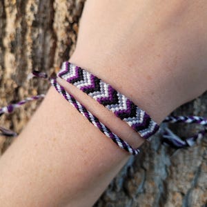 Könnte beinhalten: Zwei Freundschaftsarmbänder, eines mit einem Chevron-Muster in Schwarz, Weiß und Lila, das andere mit einem gestreiften Muster in Schwarz und Weiß.