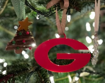 May include: A red plastic ornament shaped like the letter G hanging on a Christmas tree.