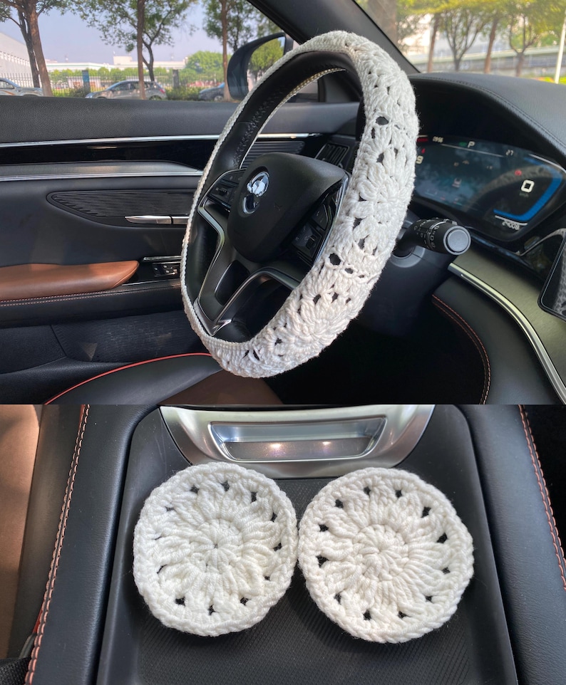 May include: White crocheted steering wheel cover and two matching coasters. The steering wheel cover has a floral design. The coasters are round and have a similar floral design.