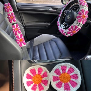 May include: A set of crocheted car accessories in pink and white with orange centers. The set includes a steering wheel cover, two seatbelt covers, and two coasters.