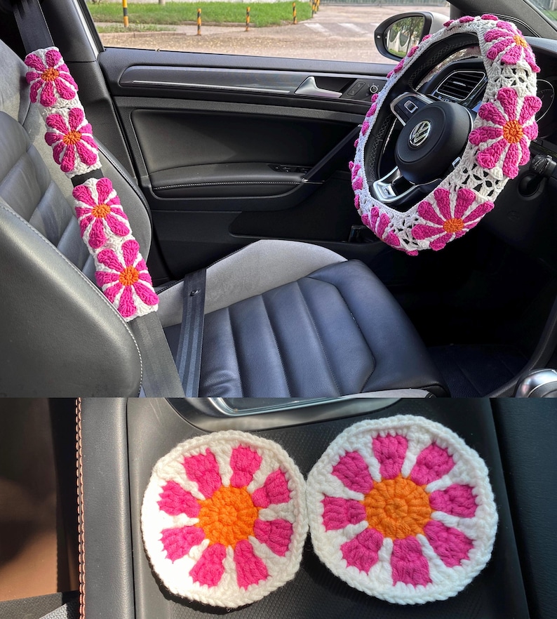 May include: A set of crocheted car accessories in pink and white with orange centers. The set includes a steering wheel cover, two seatbelt covers, and two coasters.