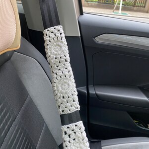 May include: White crocheted seatbelt cover with a black and white striped seatbelt.