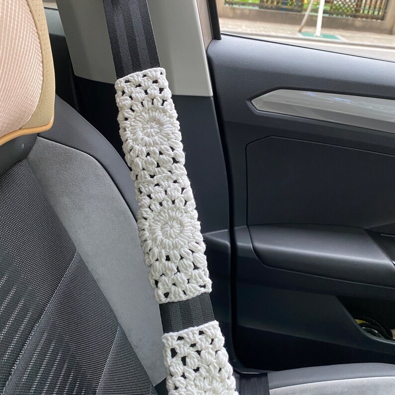May include: White crocheted seatbelt cover with a black and white striped seatbelt.
