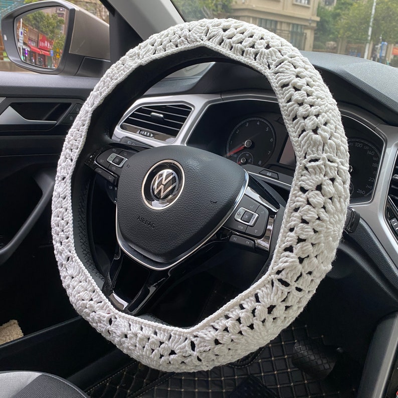 May include: White crocheted steering wheel cover. The cover is made of a delicate, open-weave pattern and is designed to fit over a standard steering wheel.