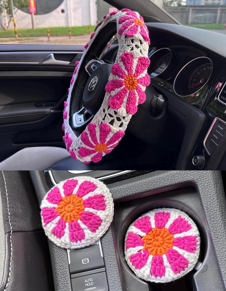 May include: A set of crocheted car accessories in pink and white with orange centers. The set includes a steering wheel cover, a gear shift knob cover, and two cup holders.