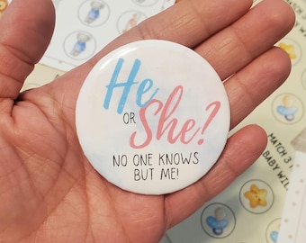 May include: A white button with the text "He or She?" in blue and pink, with the words "NO ONE KNOWS BUT ME!" in black. The button is held in a hand, with baby shower game cards in the background.
