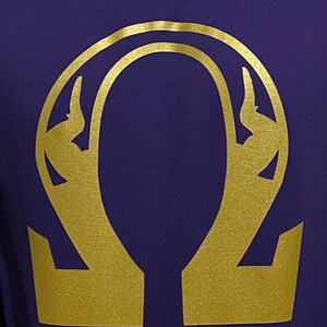 Puede incluir: Un símbolo omega de color dorado sobre un fondo morado.