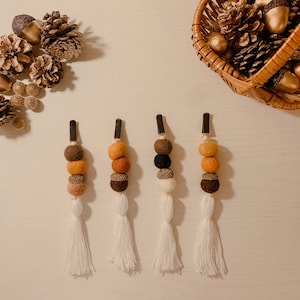 May include: Four brown, orange, and white felt ball tassel keychains with black clips. The tassels are made of white yarn.