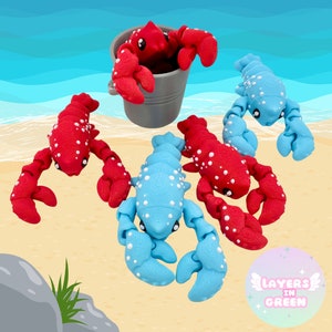 Può includere: Quattro figurine di aragosta colorate, due rosse e due blu, con punti bianchi. Le aragoste sono disposte su una superficie sabbiosa con uno sfondo blu.