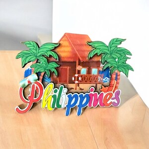 May include: A colorful wooden souvenir with the word "Philippines" in rainbow letters. The souvenir features a small hut with palm trees and a beach scene.