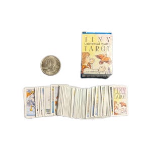 May include: A miniature "Tiny Universal Waite Tarot" deck with a quarter for size comparison. The deck includes a box with the deck name and artwork of a person and a bird. The cards are fanned out, showing their illustrated backs.