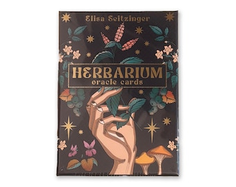 Puede incluir: Una caja negra de "Herbarium Oracle Cards" de Elisa Seitzinger. La caja presenta ilustraciones de una mano sosteniendo hojas, setas, flores y estrellas. El texto es en oro y blanco.