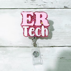 Op de afbeelding: Een roze en glitterende ER Tech badge reel met witte tekst. De badge reel heeft een doorzichtige plastic band en een metalen clip. De achtergrond is een wit houten oppervlak.