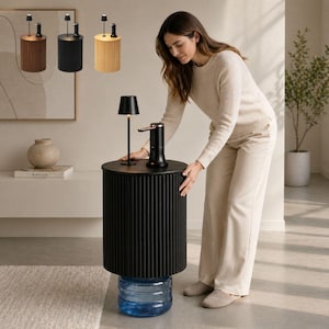 May include: A cylindrical black side table with a vertically ribbed exterior, featuring a flat top surface that holds a small black lamp and a black water dispenser pump. The table is positioned over a large, clear blue plastic water jug.