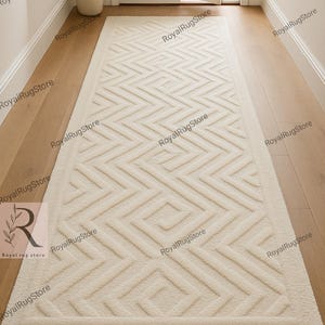 May include: Cream-colored rectangular rug with a geometric pattern, placed in a hallway with wooden flooring. The rug features a repeating zigzag design within a bordered frame, adding texture and visual interest to the space.