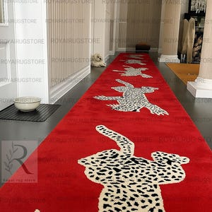 May include: A long, rectangular red runner rug featuring a repeating pattern of white and black leopard figures. The rug is positioned along a hallway floor, showcasing a vibrant red background with stylized animal motifs arranged in a sequence.