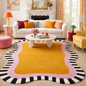 May include: A living room scene featuring a large, mustard-yellow rug with a wavy pink border and black and white striped edges. The room includes a white sofa with colorful pillows, a gold mirror, and various lamps.