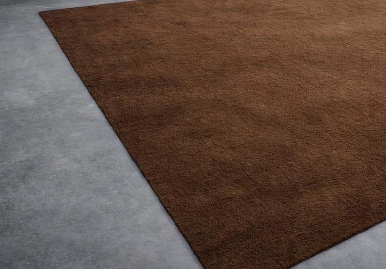 May include: A rectangular, brown rug with a soft, textured surface. The rug is placed on a gray concrete floor, with a portion of the floor visible in the image. The rug's color is a rich, warm brown.