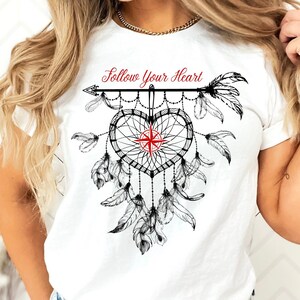Peut inclure: T-shirt blanc avec un motif de capteur de rêves noir et rouge et le texte "Follow Your Heart". Le capteur de rêves est en forme de cœur, avec des plumes et une rose des vents au centre.