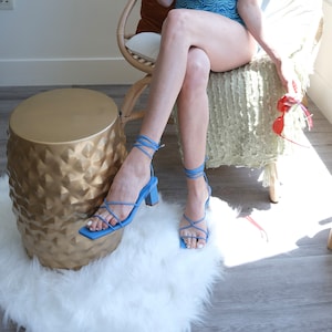 May include: A pair of blue strappy heeled sandals with a square toe. The sandals are tied up the leg with thin straps.