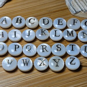 May include: White round beads with silver letters spelling out the alphabet A through Z. The beads are on a white string.
