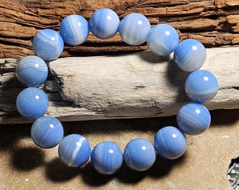 May include: A bracelet made of round, light blue beads with white swirling patterns. The beads are strung together, forming a circular shape. The bracelet is displayed on a wooden surface, showcasing the natural color variations of the beads.