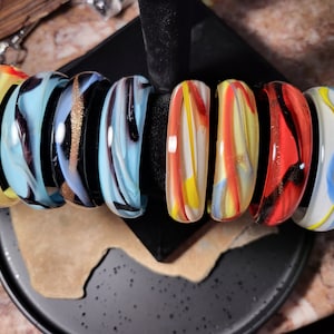 May include: A set of eight colourful glass bangles with swirling patterns in shades of blue, yellow, red, and orange.