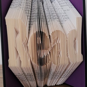 May include: A book art sculpture with the word "Hero" folded into the pages. The book is bound in a purple cover with black edges.