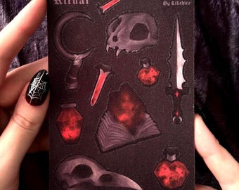 May include: A dark card featuring the word "Ritual" and occult symbols like a crescent moon, skull, dagger, and potion bottles. The card has a gothic aesthetic with red and black accents.