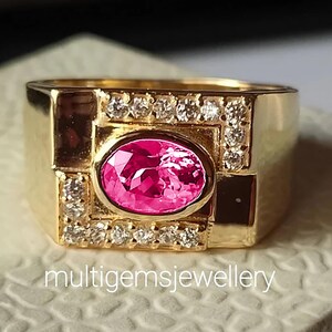 May include: A gold ring with a pink oval gemstone surrounded by smaller diamonds. The ring has a square design with a raised center.