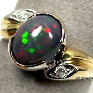 Puede incluir: Un anillo bicolor de oro y plata con una gran ópalo negro ovalado con destellos verdes y rojos. El anillo tiene detalles de diamantes y un diseño de dos tonos, mostrando una estética lujosa.