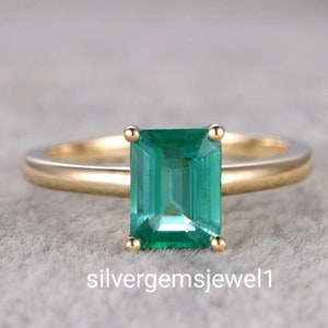 Puede incluir: Un anillo de oro con una piedra verde rectangular con talla esmeralda. El anillo tiene un diseño sencillo con una banda fina y cuatro garras que sujetan la piedra. El texto "silvergemsjewel1" es visible en la parte inferior de la imagen.