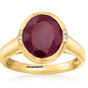 May include: A gold ring with a large oval ruby gemstone and smaller diamonds set around the ruby. The ring is engraved with the text "silvergemsjewel1".
