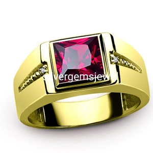 Puede incluir: Un anillo de oro con una piedra preciosa roja cuadrada grande y piedras preciosas blancas más pequeñas en la banda.