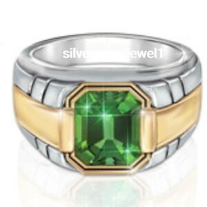 Puede incluir: Un anillo bicolor con una gran gema verde talla esmeralda. El anillo presenta una banda plateada con detalles dorados alrededor de la gema y en los laterales. El texto "silver jewel1" es visible.