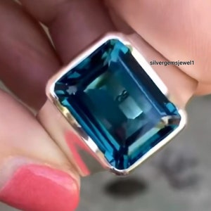 Puede incluir: Un anillo de plata con una gran piedra preciosa rectangular azul. La piedra preciosa está engastada en una banda de plata.