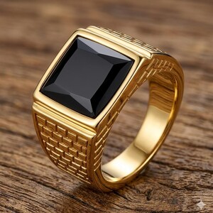 Puede incluir: Un anillo dorado con una gran piedra negra rectangular. El anillo tiene un diseño texturizado en los laterales y un acabado pulido. El anillo está sobre una superficie de madera.