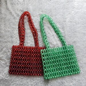 May include: Two beaded handbags, one red and one green. The bags are made of small, round beads woven together in a grid pattern. The bags have a simple, rectangular shape with two short handles.