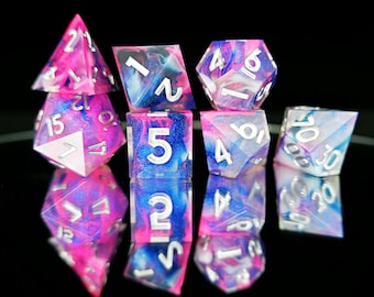 May include: A set of ten polyhedral dice in various shapes, including a d4, d6, d8, d10, d12, and d20. The dice are a mix of pink, blue, and white with silver numbering. The dice are designed for tabletop role-playing games.