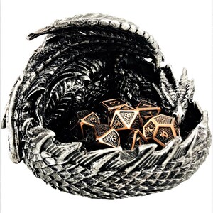 May include: A silver dragon sculpture with an open mouth, holding a set of copper and silver dice. The dragon is a dice tray for tabletop games.