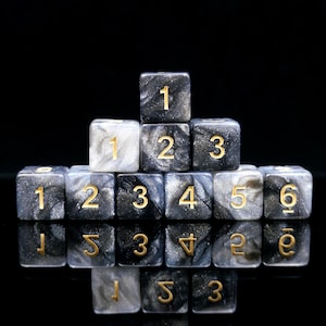 May include: A collection of marbled dice with gold numbering. The dice are arranged in a pyramid shape, with the numbers 1 through 6 visible. The dice have a black and gray color scheme.