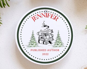 May include: A white round ornament with a green border and white polka dots. The ornament features a black and white illustration of a stack of books with a coffee cup on top. The text "JENNIFER PUBLISHED AUTHOR 2022" is printed in red and black.
