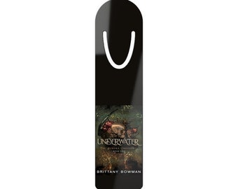 May include: Black bookmark with a white bookmark tab. The bookmark features a book cover with a skull and flowers on a dark green background. The book cover text reads "UNDERWATER THE AURORA CHRONICLES BOOK ONE BRITTANY BOWMAN".
