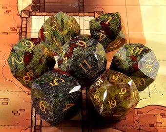 Peut inclure: Un ensemble de sept dés polyédriques avec un motif tacheté vert et rouge. Les dés ont des chiffres dorés et sont disposés sur une surface ressemblant à une carte. Idéal pour les jeux de rôle.