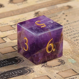 May include: A purple gemstone dice with gold numbers 3, 6, and C. The dice is on a brown surface with a grid pattern.